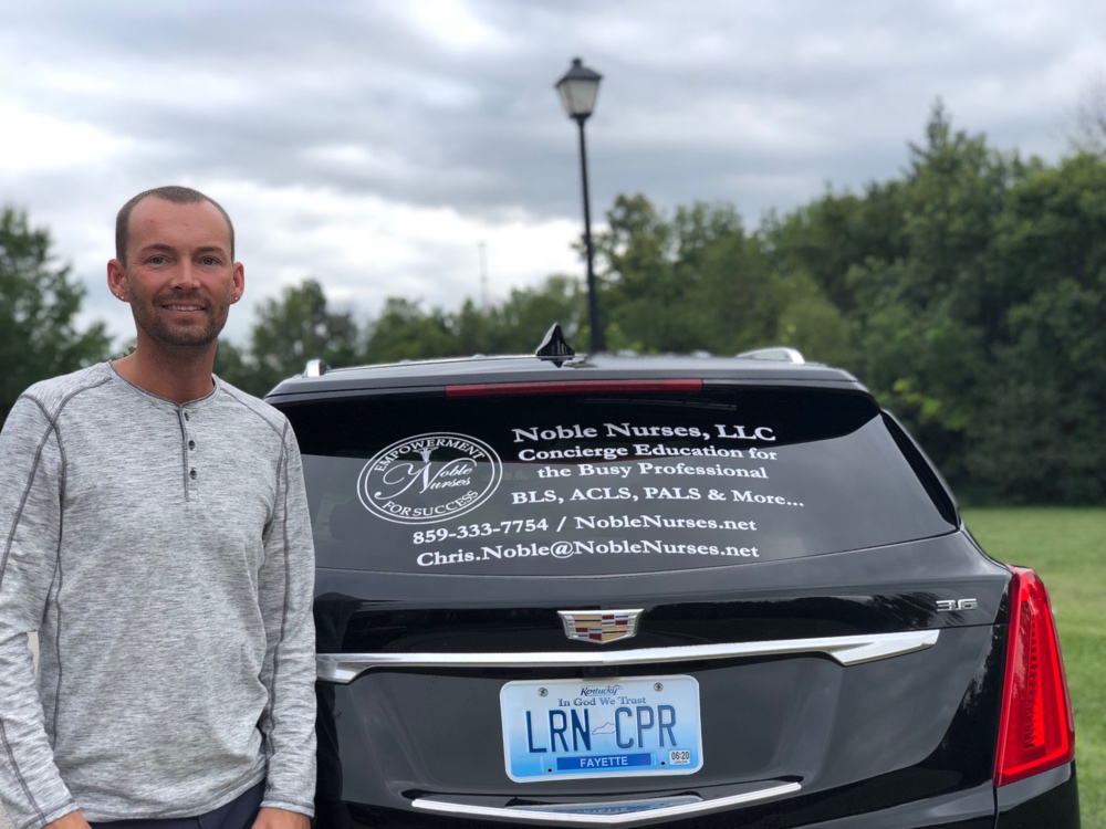 A photo of Chris Noble standing in front of his black Cadillac SUV. The rear window has a large Noble Nurses decal. The Kentucky license plate has the letters L R N C P R.